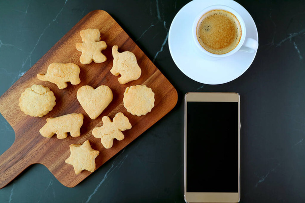 Roztomilé zvíře tvarované cookie s šálkem kávy a prázdné obrazovky Smartphone na černém mramorovém stole - Fotografie, Obrázek
