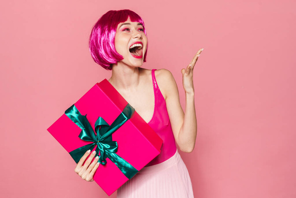 Immagine di felice bella donna in parrucca ridere e tenere scatola regalo isolato su sfondo rosa
 - Foto, immagini