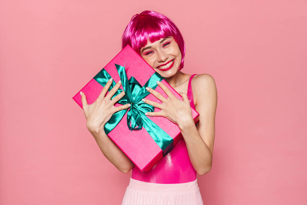 Image of happy beautiful woman in wig smiling and holding gift box isolated over pink background - Valokuva, kuva