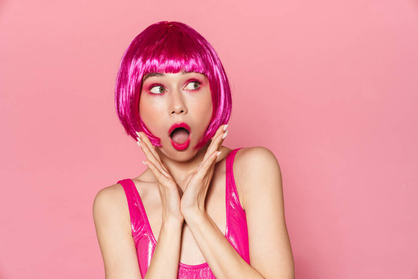 Image of young party girl wearing wig expressing surprise at camera isolated over pink background - Фото, изображение