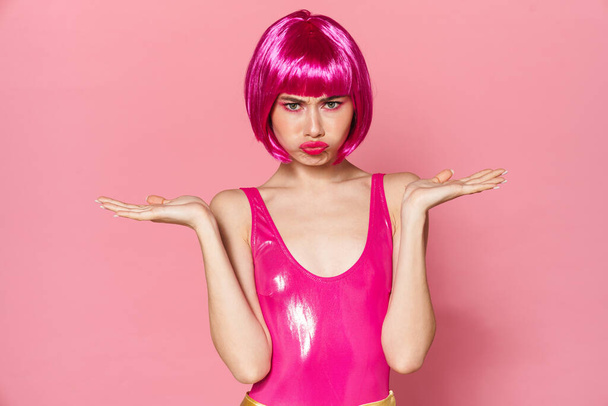 Image of displeased party girl wearing wig holding copyspace and looking at camera isolated over pink background - Foto, imagen