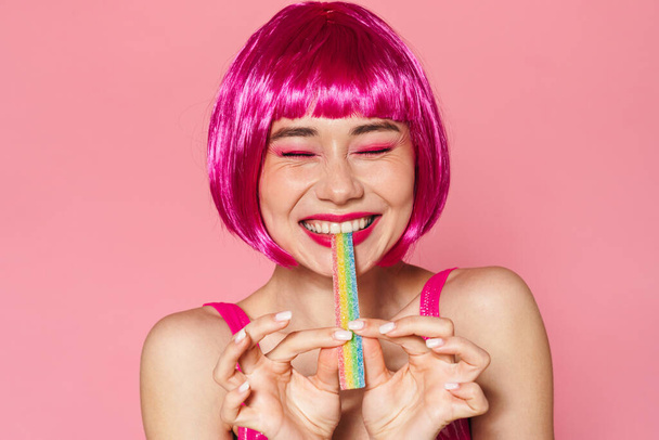 Image of joyful beautiful woman in wig making fun with marmalade isolated over pink background - 写真・画像