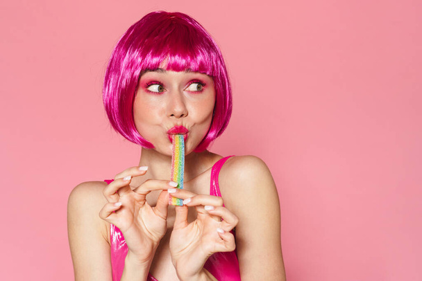 Image of joyful beautiful woman in wig making fun with marmalade isolated over pink background - Foto, Imagen