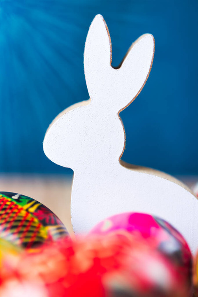 Easter bunny figurine with colorful eggs. Warm sunlight flare. Blue background. - Photo, Image
