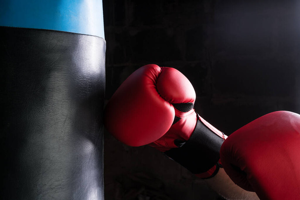 Hombre duro golpeando saco de boxeo con guante de boxeo. Aspecto de iluminación de contraste
. - Foto, Imagen