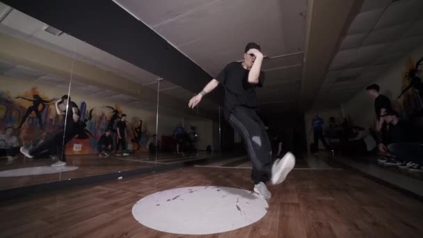 Videó egy aktív fiatalemberről, aki hip-hop koreográfiát táncol és megtörik. Más táncosok állnak a közelben. Tánciskola. Fogalma javítása break tánc technika. Ifjúsági szubkultúra. Kortárs koreográfia. Lassú mozgás.  - Felvétel, videó