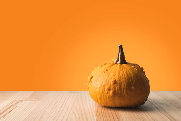 Halloween pumpkin on a wooden table with orange background. Large copy space on the left. - Photo, Image