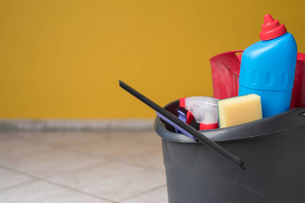 House spring cleaning items or supplies in a bucket on a tile floor. Copy space on the left. - Photo, Image