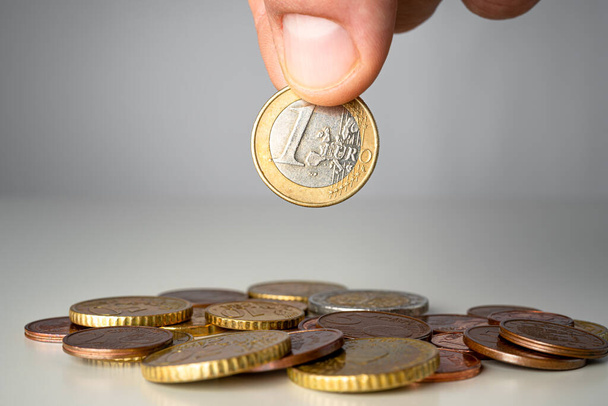 Καυκάσιος που κρατάει το ευρώ πάνω από το σωρό των νομισμάτων. Εξοικονόμηση χρημάτων αφηρημένη έννοια. - Φωτογραφία, εικόνα