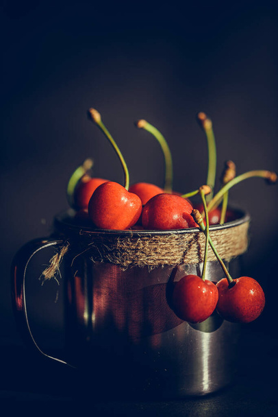 Ripe and juicy cherries in old metal cup on the dark rustic background. Selective focus. Shallow depth of field. - Photo, Image