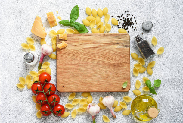 Food background with place for text. Cutting board, raw pasta, spices, parmesan, basil crawling around. Wooden board. Top view. - Foto, immagini