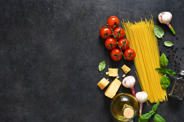 Ingredients for making pasta. Raw spaghetti with tomato and basil on a black background. View from above. - Foto, immagini