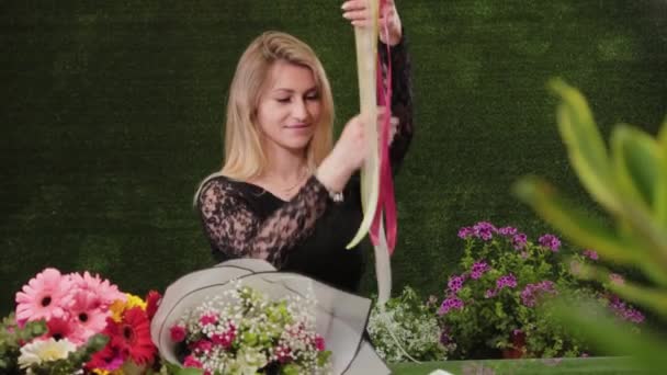 Professional woman florist unwinds the red ribbon, cuts it with scissors to pack the bouquet. - Footage, Video