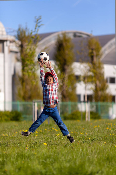 Kleiner Junge Torwart springt, um einen Fußball zu fangen. Junge afrikanische amerikanische Fußballspieler beim Training auf einem Rasenplatz. - Foto, Bild