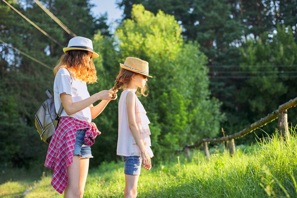 Verano, niños felices caminando disfrutando de vacaciones en la naturaleza, hermana mayor trenzas su cabello más joven
 - Foto, Imagen