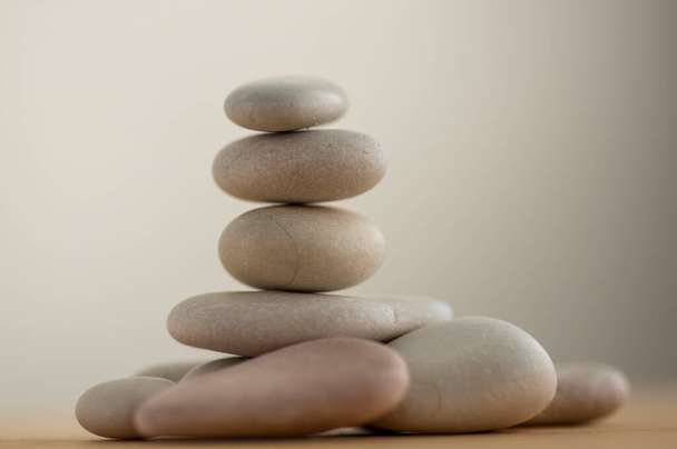 One simplicity stones cairn isolated on white background, group of light gray pebbles built in tower, wooden table, harmony and balance - Zdjęcie, obraz