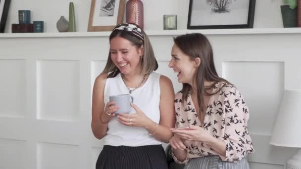 Two women laugh and chat. Group of friends using smart phones and digital tablet. Cheerful millenial women using and talking on social networks to group of multiracial friends. - Filmati, video