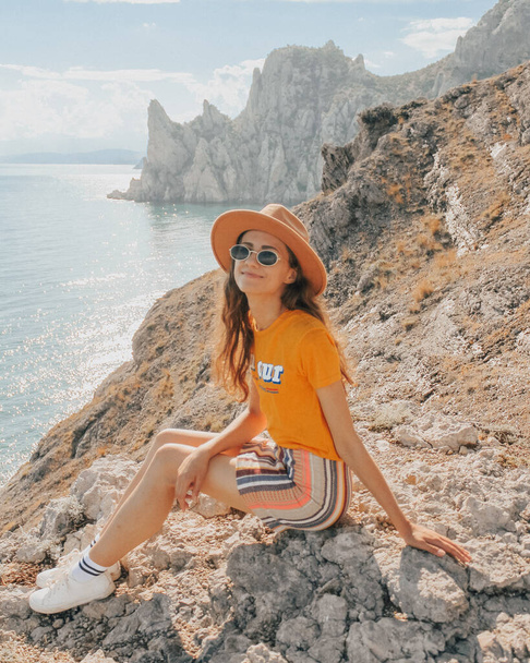 Beautiful girl in a hat on a summer vacation in the mountains on nature. Blue sky and sea. - Foto, Imagen