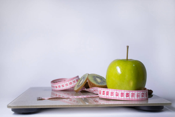Fita métrica vermelha, maçã, kiwi em escalas de banheiro bege. Dieta e vida saudável, perda de peso, conceito de esporte. Vista superior. Espaço para cópia. Isolado. Fundo branco
 - Foto, Imagem
