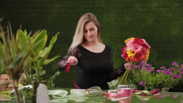 Profesionální žena květinářství odvíjí červenou stuhu, řeže ji nůžkami balit kytice. - Záběry, video