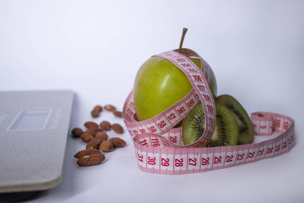 Nastro rosso di misurazione, mela, kiwi e mandorle vicino alle squame del bagno. Dieta e vita sana, perdita di peso, concetto di sport. Ricevuto. Isolato. Fondo bianco
 - Foto, immagini
