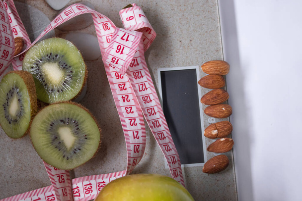 Rode meetlint, appel, kiwi en amandelen op beige badkamerweegschalen. Dieet en gezond leven, verlies gewicht, sport concept. Bovenaanzicht. Begrepen, ruimte. Geïsoleerd. Witte achtergrond - Foto, afbeelding