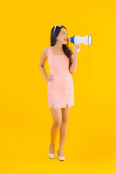 Retrato bela jovem mulher asiática falar alto com megafone no amarelo isolado fundo
 - Foto, Imagem