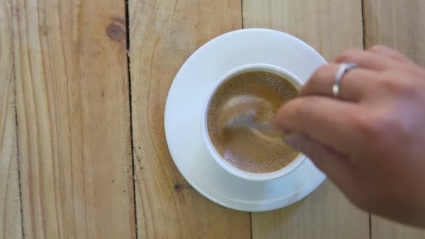 スプーンでカップに人の手ステアリングコーヒーのトップビュー。木製の背景にカップホットブラックコーヒーの朝食。映像B-rollシーン4k.自家製コーヒー.  - 映像、動画