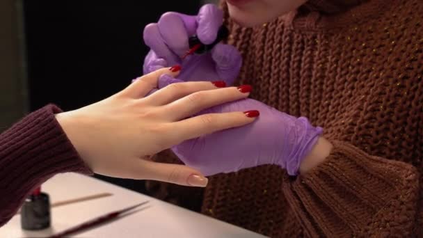 マニキュリストは、薄い赤の色で女の子の爪をペイントします。美容室でのマニキュアプロセス。ピンクの手袋のマニキュリスト - 映像、動画