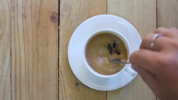 Blick von oben auf Person handlenkenden Kaffee in einer Tasse mit Löffel. Frühstücksfrühstück mit einer Tasse heißen schwarzen Kaffee auf Holzuntergrund. Filmmaterial B-Roll Szene 4k. hausgemachter Kaffee.  - Filmmaterial, Video