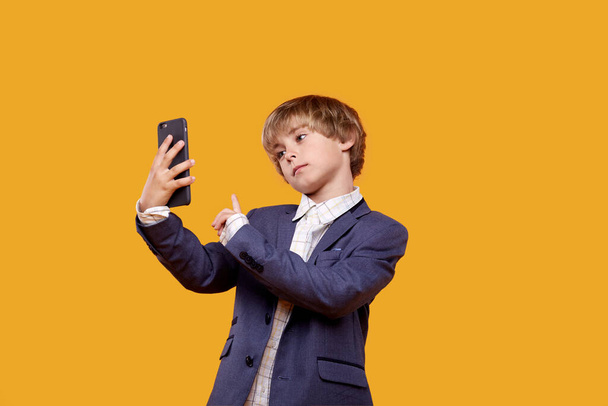 Cute beautiful little boy takes a selfie with a mobile phone in his hands. - Zdjęcie, obraz
