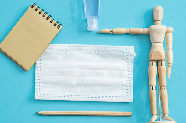 wooden mannequin of a woman and medicine mask, sanitizer, notebook and pencil. Work at home. Flat lay on a blue background. - Foto, immagini