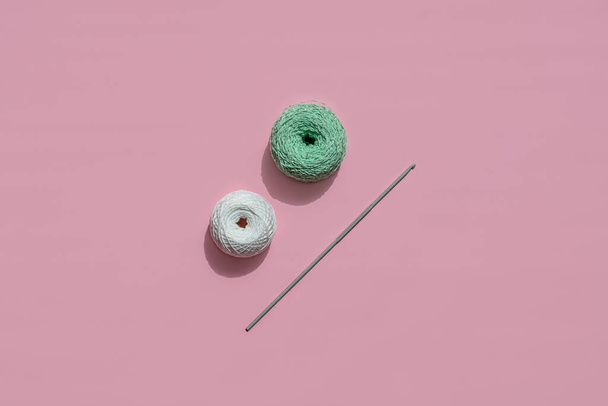 two balls of yarn and a hook. Green and white on a pink background. - Fotó, kép