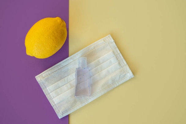 lemon, medical mask and sanitizer on a yellow-violet background. Summer during Coronavirus crisis concept  - Photo, image