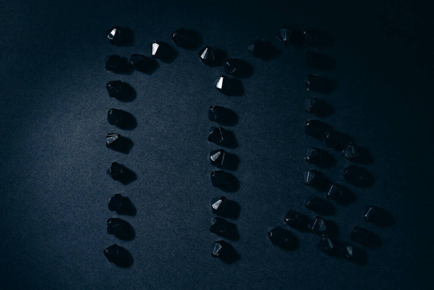 Symbol des Tierkreiszeichens Jungfrau aus schwarzen Steinen auf schwarzem Hintergrund. Niedrige Dunkelziffer. Vignettenbeleuchtung. Horoskop-Thema - Foto, Bild