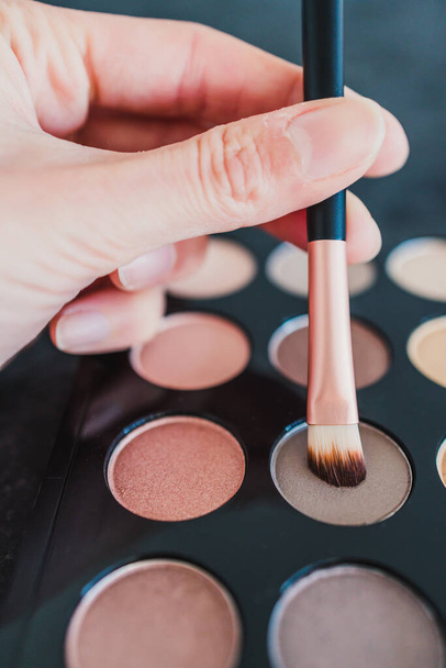 cosmetics and beauty industry concept, close-up of eyeshadow palette with neutral nude tones and hand holding brush on it  - Photo, Image