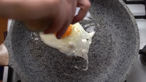 Chef seasons a Frying egg, sunny side up, with ground pepper in a small frying pan over an gas burning stove - 映像、動画