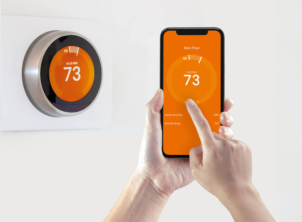 Een persoon die een smartphone-applicatie gebruikt om de kamertemperatuur op te warmen met een draadloze slimme thermostaat op een witte achtergrond. - Foto, afbeelding