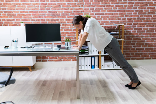 Side View Of A Young Businesswoman Doing Push Up On Office Desk - Foto, Imagem