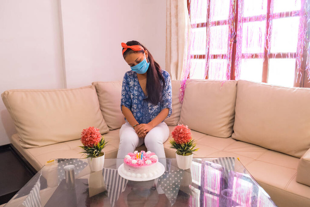 Una mujer triste con una máscara para prevenir el virus y en su fiesta de cumpleaños. Fiesta de cumpleaños sola. Quedarse en casa en cuarentena
 - Foto, Imagen
