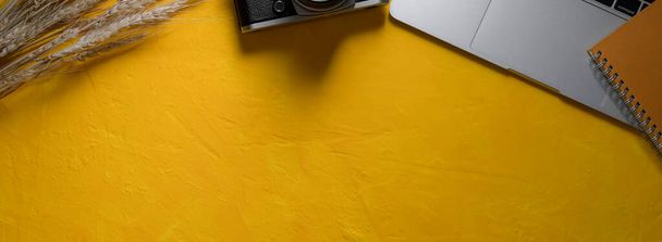 Vista superior del espacio de trabajo creativo con computadora portátil, cámara, libro de programación y espacio de copia sobre fondo de hormigón amarillo
 - Foto, imagen