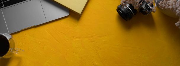 Horní pohled na kreativní pracoviště s notebookem, fotoaparátem, diářem, dekoracemi a kopírovacím prostorem na žlutém betonovém pozadí - Fotografie, Obrázek