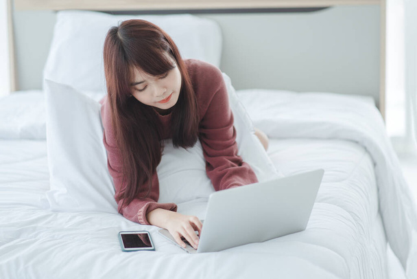 nő dolgozik egy laptop ül az ágyon a házban. - Fotó, kép