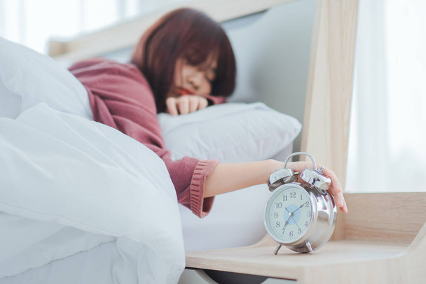 Waking up in the morning on time,alarm clock standing on bedside table going to ring early morning to wake up woman in bed sleeping in background - 写真・画像