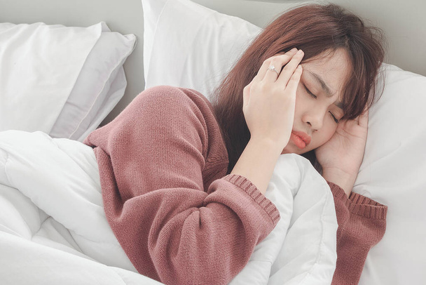 Asyalı kadın beyaz yatak odasında sabah yatakta baş ağrısı ve rahatsızlık hisseder. Kadın sağlığı anlayışı.. - Fotoğraf, Görsel