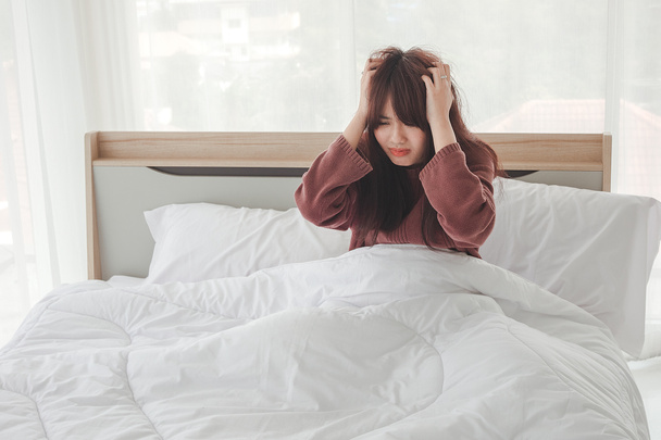 Asian woman feel headaches and discomfort on bed in white bedroom morning.Concept of women's health care. - Photo, Image