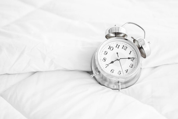A alarm clock placed on a white mattress in the morning light with copy space.Closeup black alarm clock on white mattress - Photo, Image