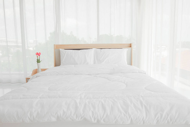Interior del dormitorio con cama y flores en la mesa. interior del dormitorio blanco con cama doble en un piso
 - Foto, Imagen