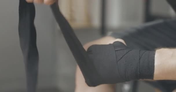 Close-up of male Caucasian hands applying boxing bandage. Unrecognizable adult sportsman wrapping wrist with black tape in gym. Sport, martial arts, lifestyle. Cinema 4k ProRes HQ. - Filmagem, Vídeo