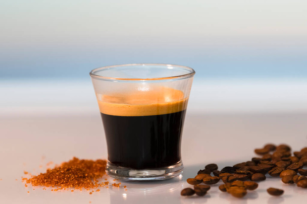 Közelkép egy eszpresszó körül barna cukor és pörkölt kávébab egy üvegasztalon egy nem fókusz háttér. Pihenés és kávé koncepció. - Fotó, kép